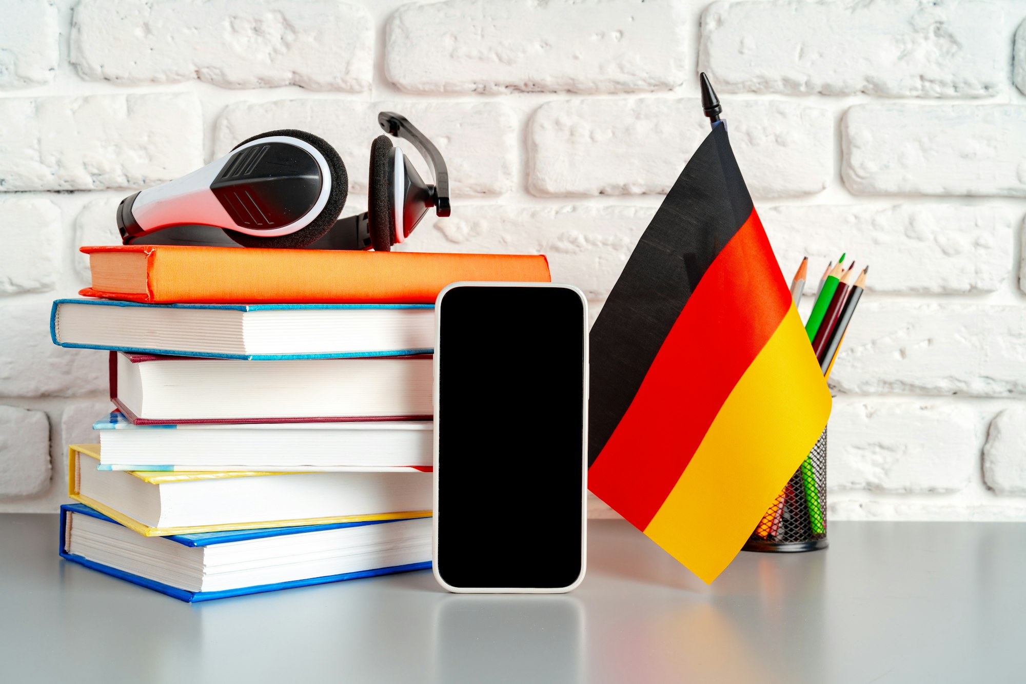 Stack of books and flag of Germany on desk. German language learning concept