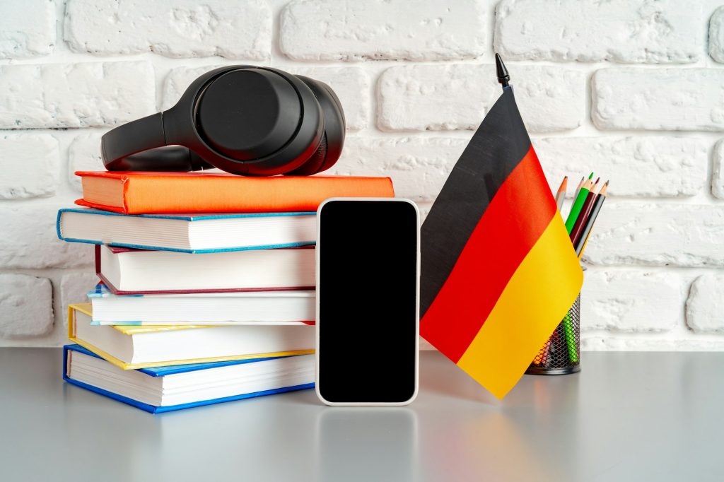 Stack of books and flag of Germany on desk. German language learning concept