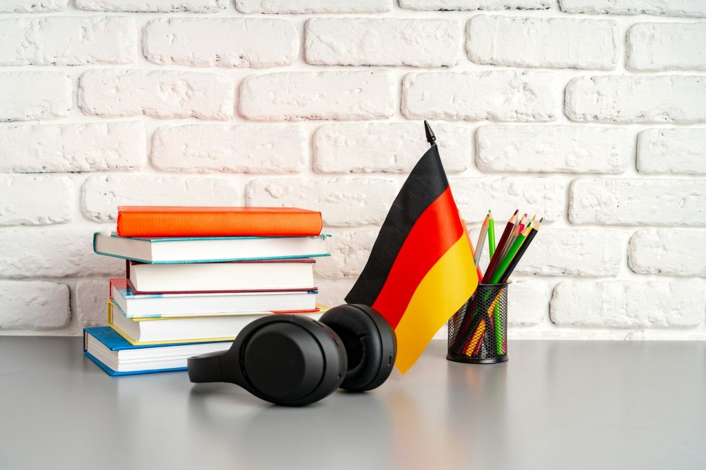 Stack of books and flag of Germany on desk. German language learning concept